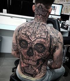 a man with tattoos on his back sitting in front of a computer desk