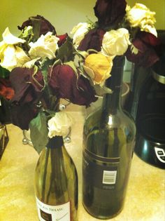 two wine bottles with flowers in them sitting on a counter