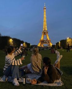 three people sitting on the grass in front of the eiffel tower at night