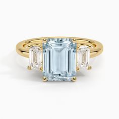 Aquamarine Luxe Rhiannon Three Stone Diamond Engagement Ring (3/4 ct. tw.) - 18K Yellow Gold. Two luxurious emerald-cut diamonds rest alongside the center gemstone in this classic, sophisticated ring (3/4 total carat weight). Earth Engagement Rings, Emerald Cut Aquamarine Ring, Moissanite Engagement Ring Rose Gold, Three Stone Diamond Rings Engagement, Three Stone Diamond Ring, Emerald Cut Rings, Aquamarine Engagement Ring, Three Stone Diamond, Emerald Engagement Ring Cut