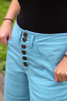 a woman wearing blue shorts with buttons on the side and her hand in her pocket