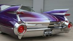 an old purple car parked in front of a garage door with the hood up and tail lights on