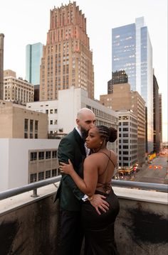 a man and woman embracing each other on top of a roof in front of tall buildings