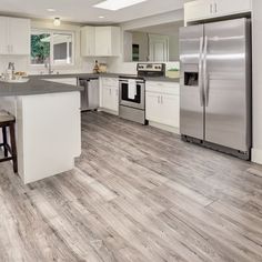 a large kitchen with white cabinets and stainless steel appliances, along with hardwood flooring