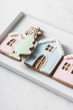 three decorated cookies sitting on top of a white tray next to each other in the shape of houses