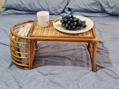 a wicker coffee table with a plate of grapes and a cup on it sitting on a bed