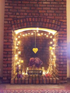 a fire place with candles and flowers on it in front of a brick fireplace that has a heart hanging from the mantle