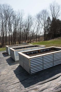 several raised garden beds on a wooden deck in the middle of a field with bare trees behind them