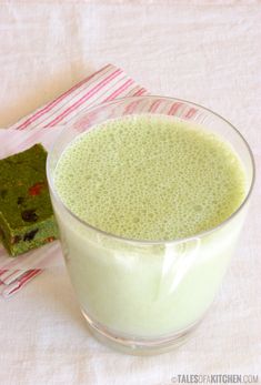 a glass filled with green liquid next to a piece of cake