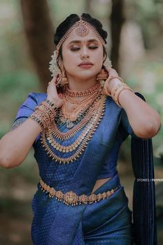 a woman in a blue sari with gold jewelry on her neck and hands behind her head