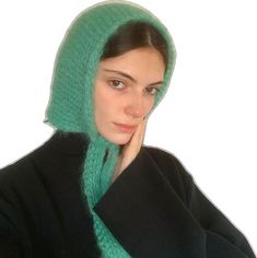 a woman wearing a green knitted hat with a hood on her head and hands under her chin