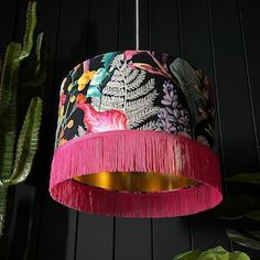 a pink lamp hanging from a ceiling next to a cactus