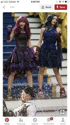 two women dressed in costumes standing on the side of a pool with water splashing around them