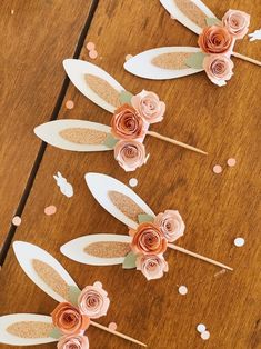 three paper flowers on sticks with confetti and polka dots scattered around them, sitting on top of a wooden table