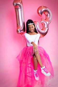 a woman in a pink tutu and white top sitting on the floor with balloons