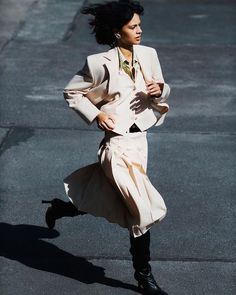 a woman is running down the street wearing a suit and tie with her hair blowing in the wind