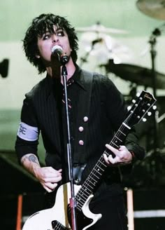 a man with black hair holding a white guitar in front of a microphone on stage