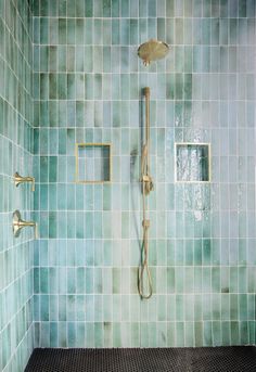 a bathroom with green tile and gold fixtures on the shower head, hand held by a brass faucet