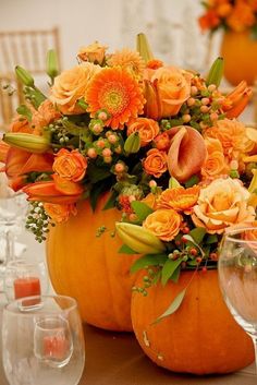 an arrangement of orange flowers and greenery sits in a pumpkin shaped centerpiece on a table