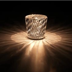 a glass candle holder sitting on top of a wooden table next to a black background