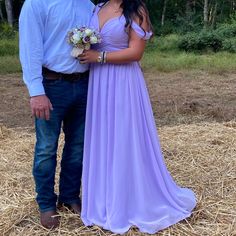 a man standing next to a woman in a purple dress on top of dry grass