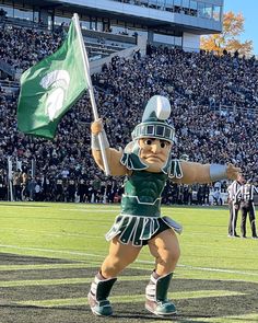 a mascot holding a flag on top of a field in front of a crowd at a football game