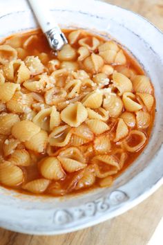 a white bowl filled with pasta and sauce on top of a wooden table next to a spoon