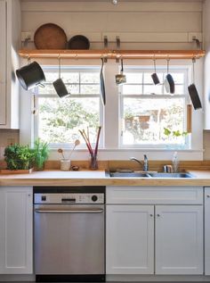 a kitchen with pots and pans hanging from the window above the sink, next to a dishwasher