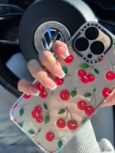 a woman's hand holding a phone case with cherries on it, in front of a steering wheel