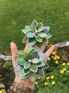 a person's hand holding up a flower made out of stained glass and metal