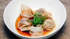 a white bowl filled with dumplings covered in sauce and garnished with green onions