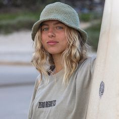 a woman holding a surfboard in her hands and wearing a hat on top of her head