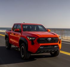 an orange toyota pickup truck driving down the road near the ocean and beach side by side