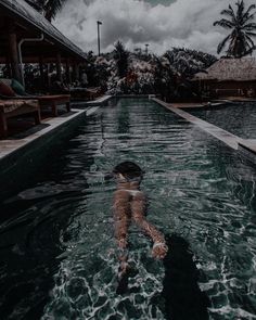 a person swimming in a pool surrounded by palm trees and cloudy skies with dark clouds