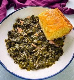 a white plate topped with greens next to a piece of bread on top of a purple towel