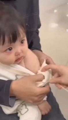 a woman holding a baby wrapped in a white towel while another person holds it up