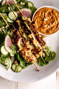 chicken skewers and salad on a white plate with peanut sauce in the background