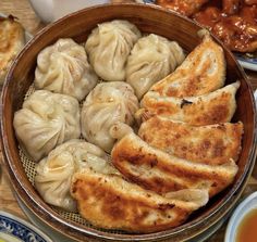 a wooden bowl filled with dumplings on top of a table next to other dishes