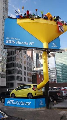 a yellow car is parked under a sign with people on it in front of some tall buildings