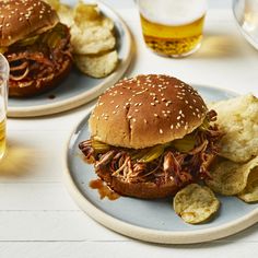 two plates with pulled pork sandwiches and potato wedges next to glasses of beer on the table