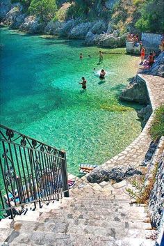 people are swimming in the clear blue water near some steps leading to an iron gate