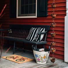 a bench sitting on the side of a red house next to a rug and potted plant