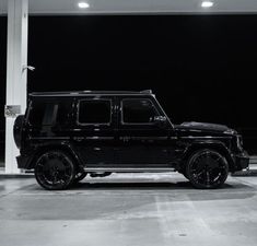 a black mercedes g - class parked in a parking garage with lights on at night