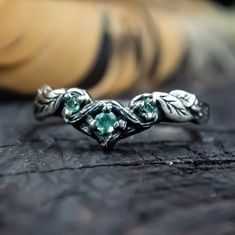 a close up view of a ring with green stones on the side and leaves in the middle