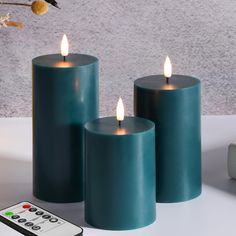 three teal colored candles sitting next to a remote control