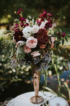 a vase filled with lots of flowers on top of a white table covered in greenery