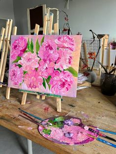 an easel with pink flowers on it and paintbrushes in front of it