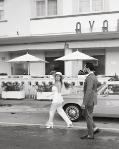 a man and woman crossing the street in front of a hotel