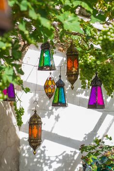 colorful stained glass hanging from the side of a white stucco wall next to green leaves