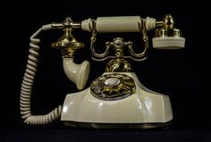 an old - fashioned white phone with gold accents sits on a black background